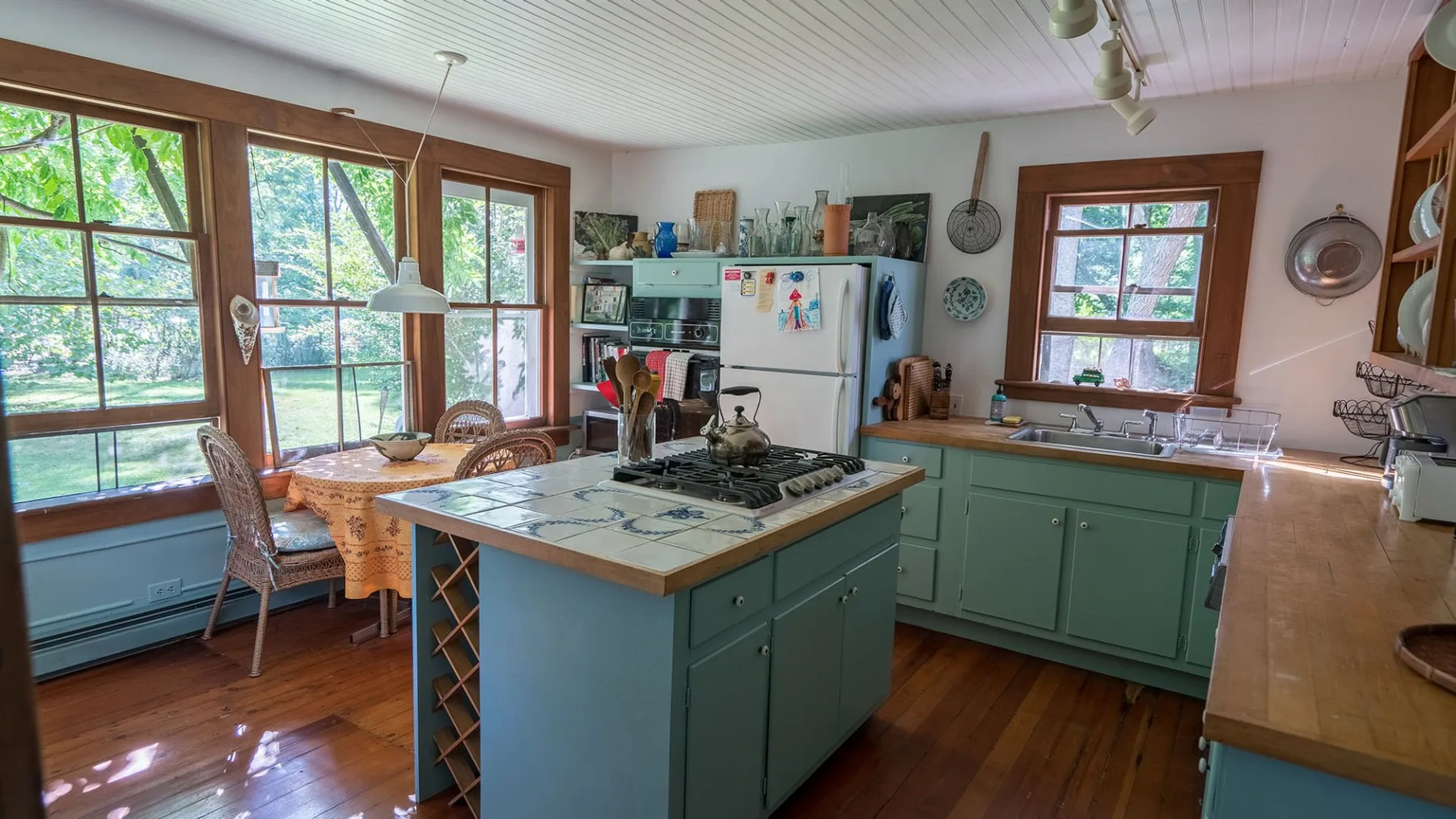 A kitchen with a central island, green cabinets, and large windows.