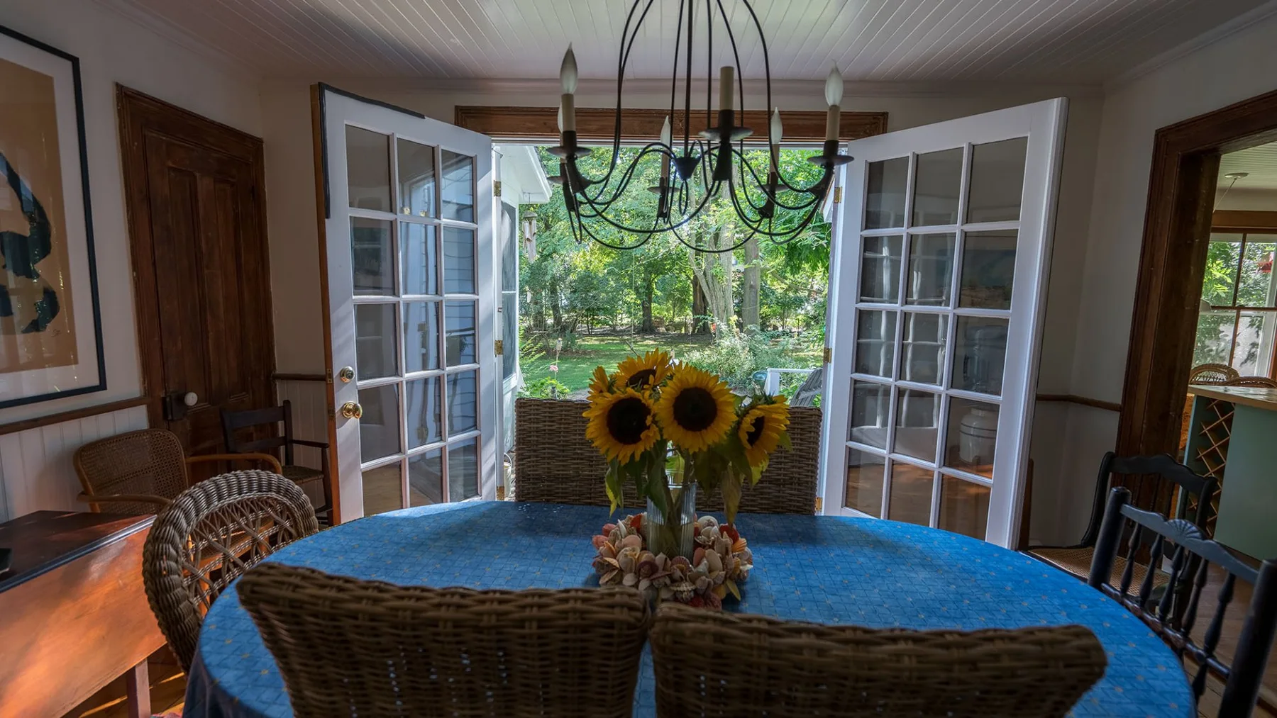 A dining area with a round table, chairs, and open glass doors to a garden.