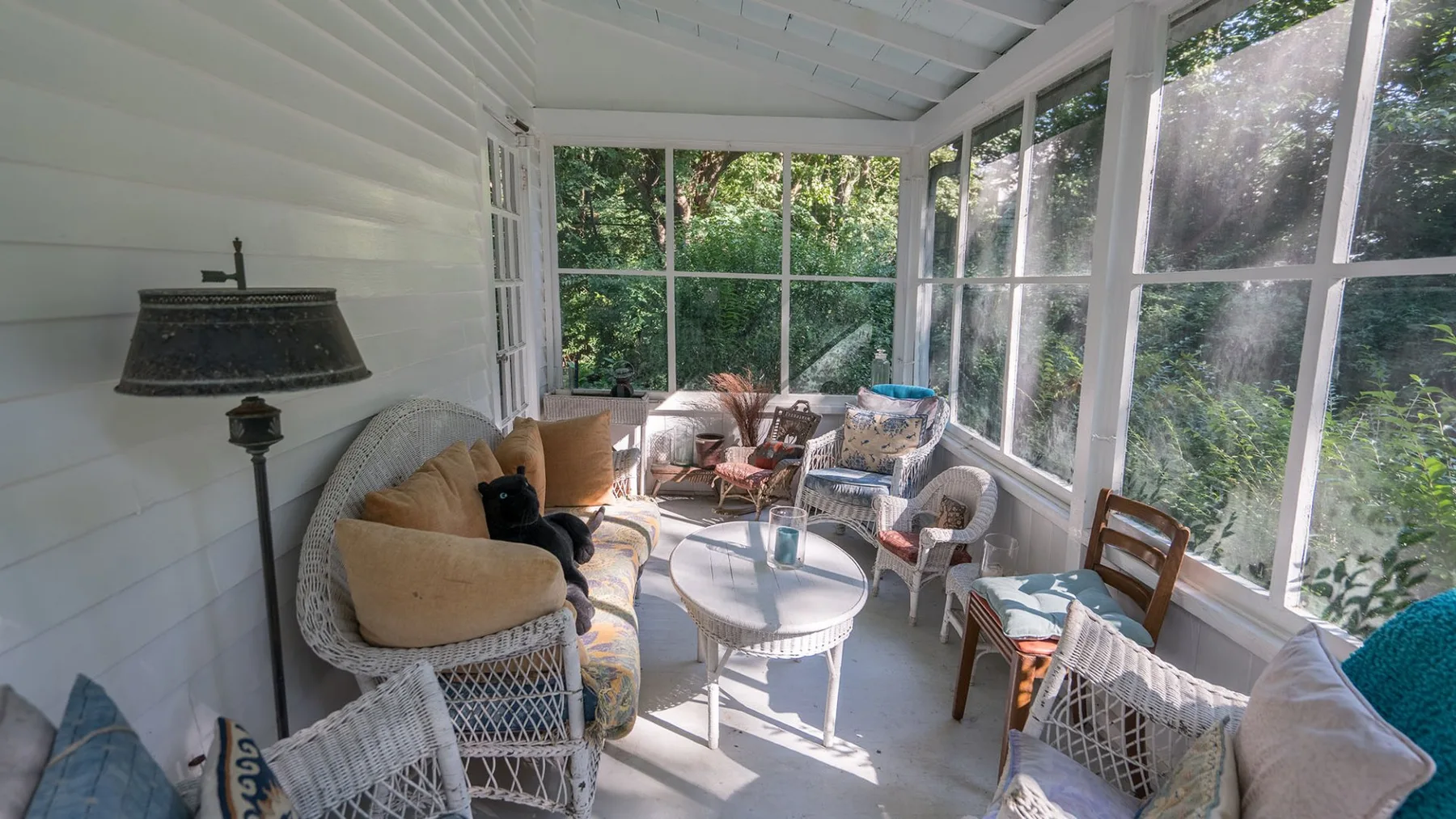 A bright enclosed sunroom has wicker seating around a small round table.