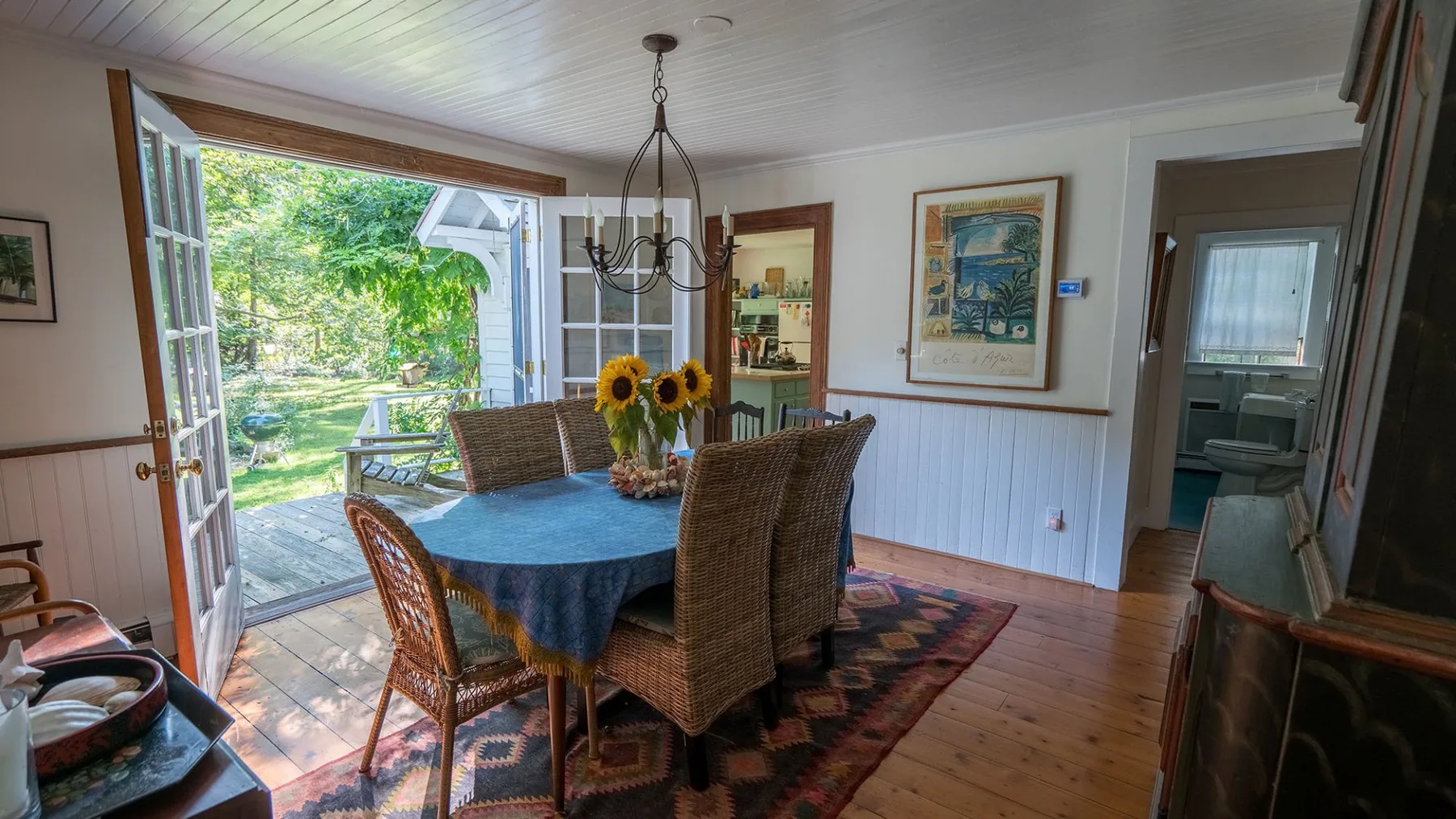 A dining room with a table and wicker seating beside open doors to a garden.