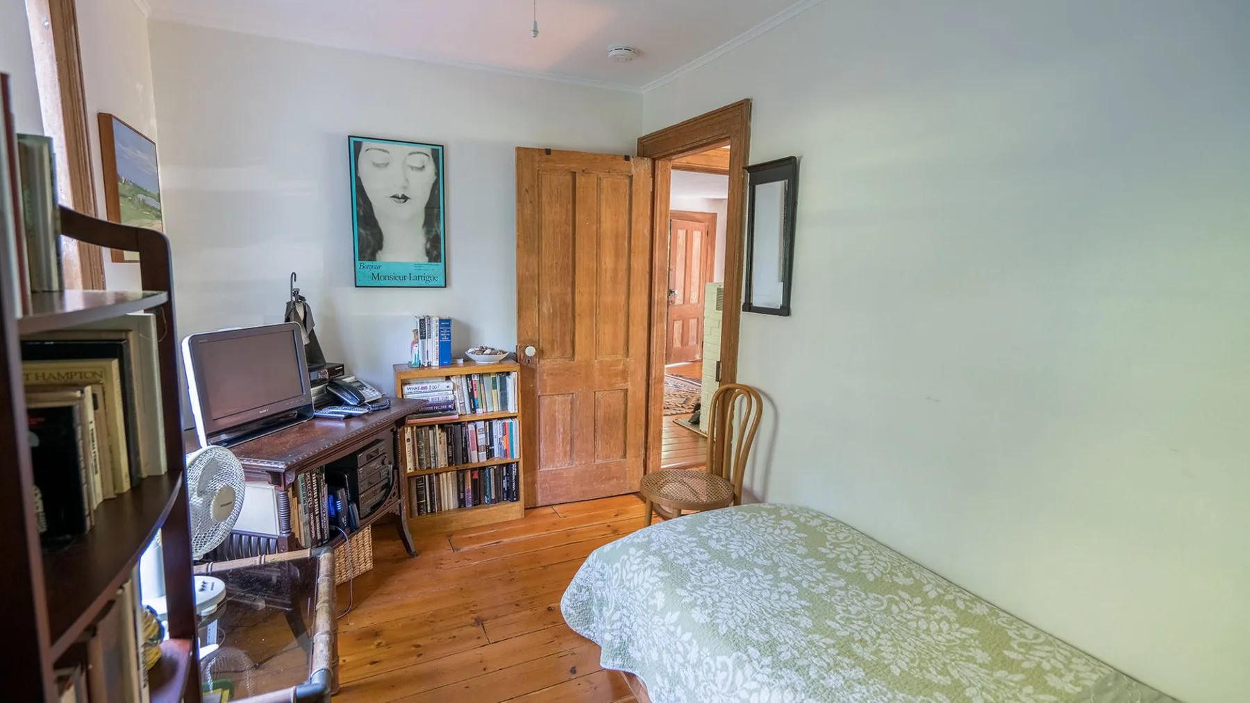 A bedroom with a bed, desk, and an open wooden door.