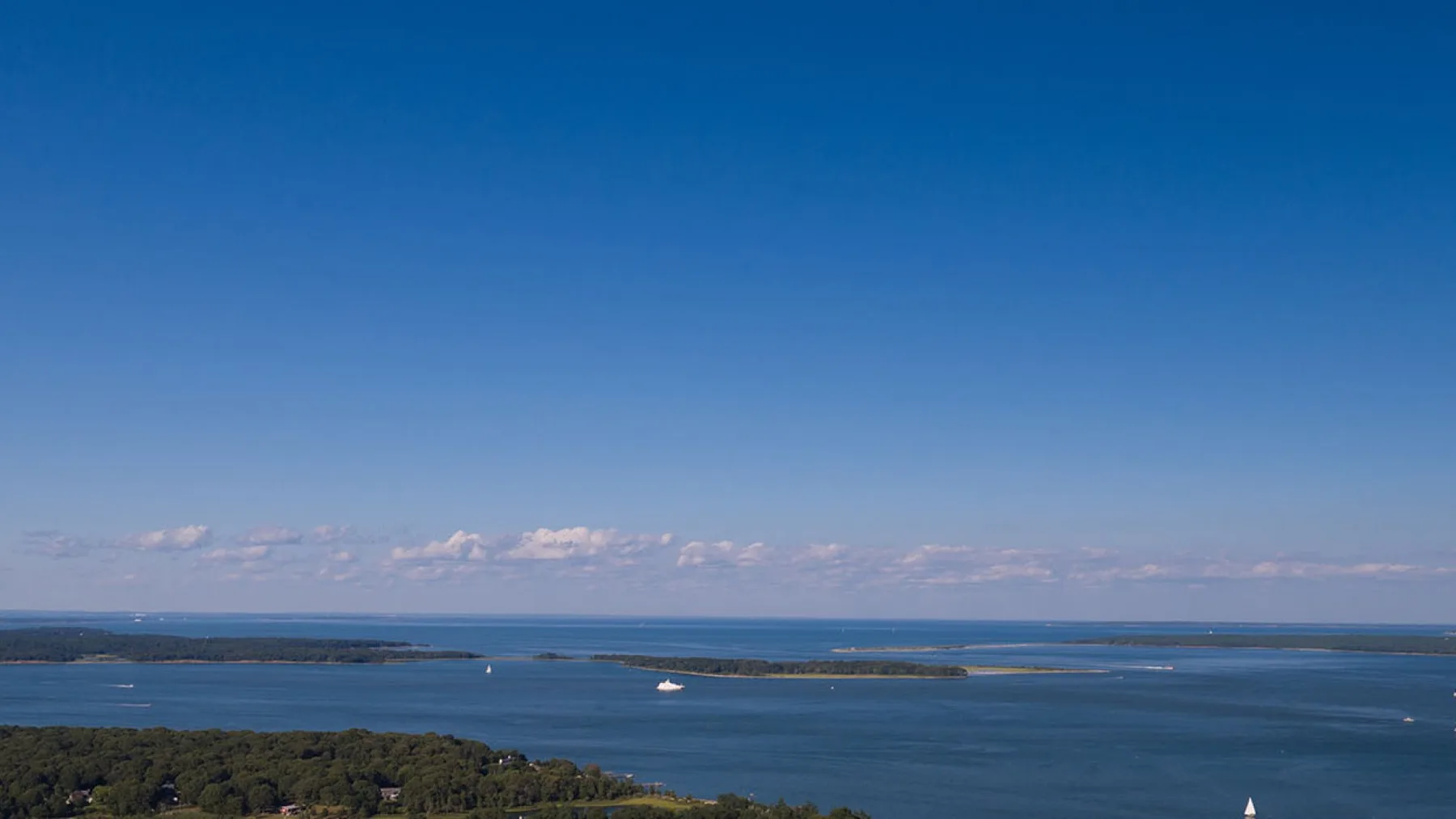 A broad expanse of blue water stretches toward a low, tree-lined shore.
