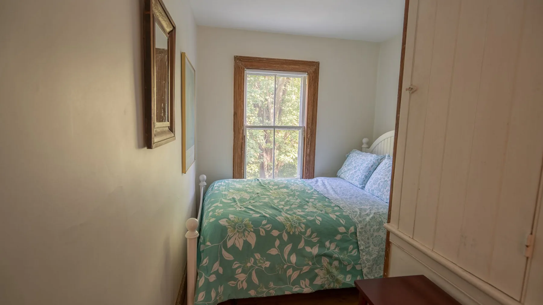 A bedroom with a bed covered in a green floral bedspread beside a window.