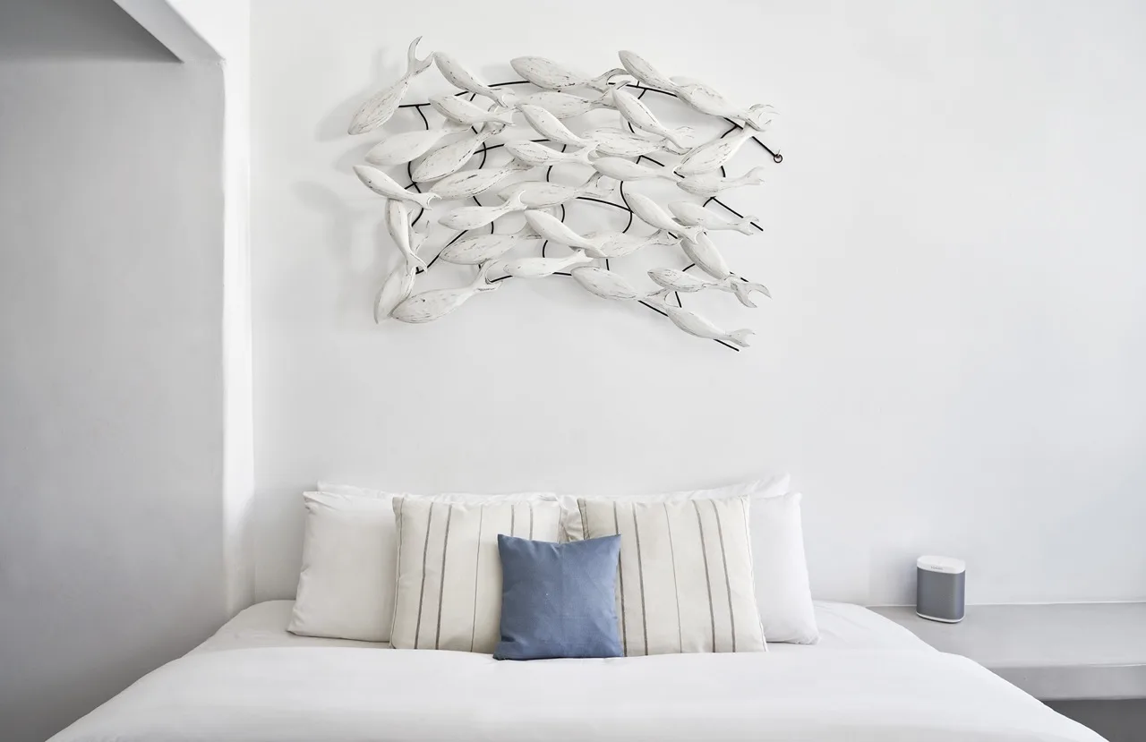 A bedroom with white bedding and a blue accent pillow beneath wall art.