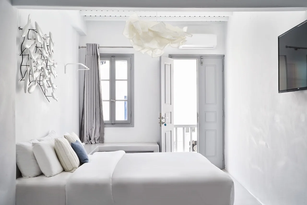 A bright bedroom with a white bed beside a window and open doorway.