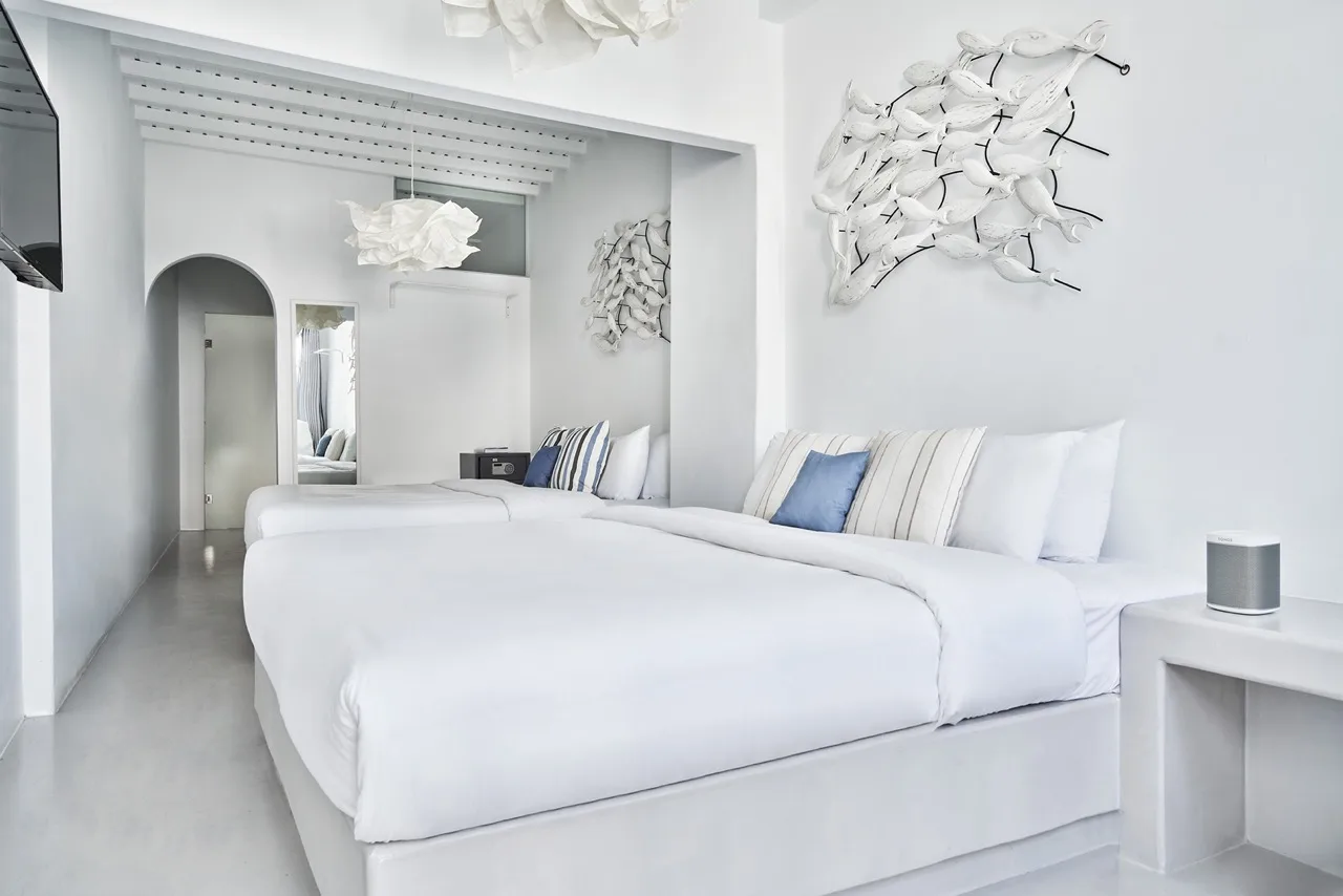 A bright bedroom with white bedding and sculptural wall decor.