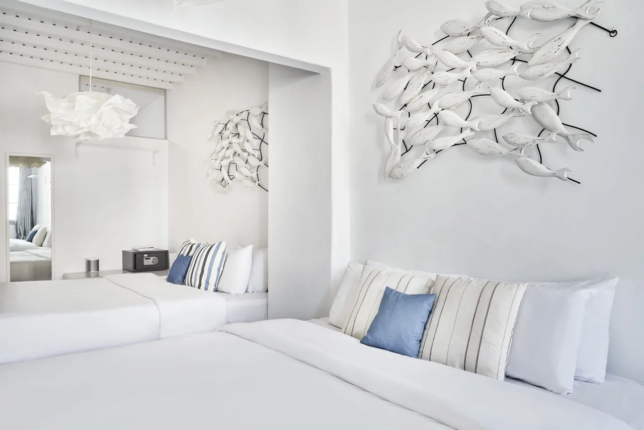 A bright bedroom with white beds, striped pillows, and sculptural wall art.