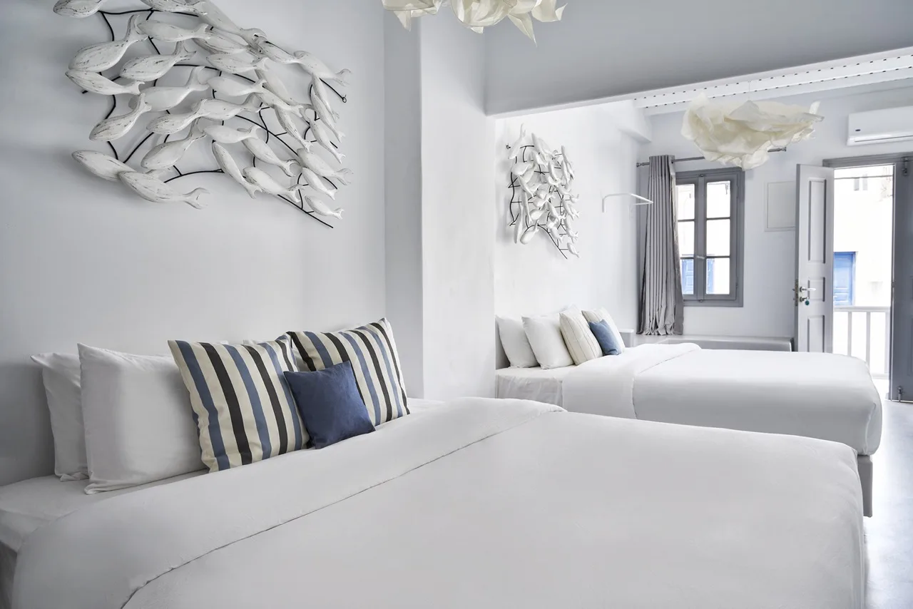 A bright bedroom with white beds, striped pillows, and fish-shaped wall art.