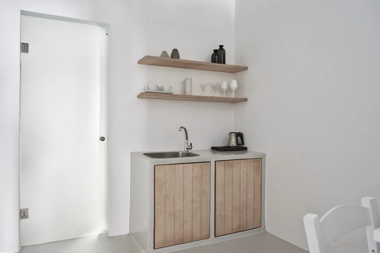 A compact kitchenette with wood-front cabinets, a sink, and open shelves.