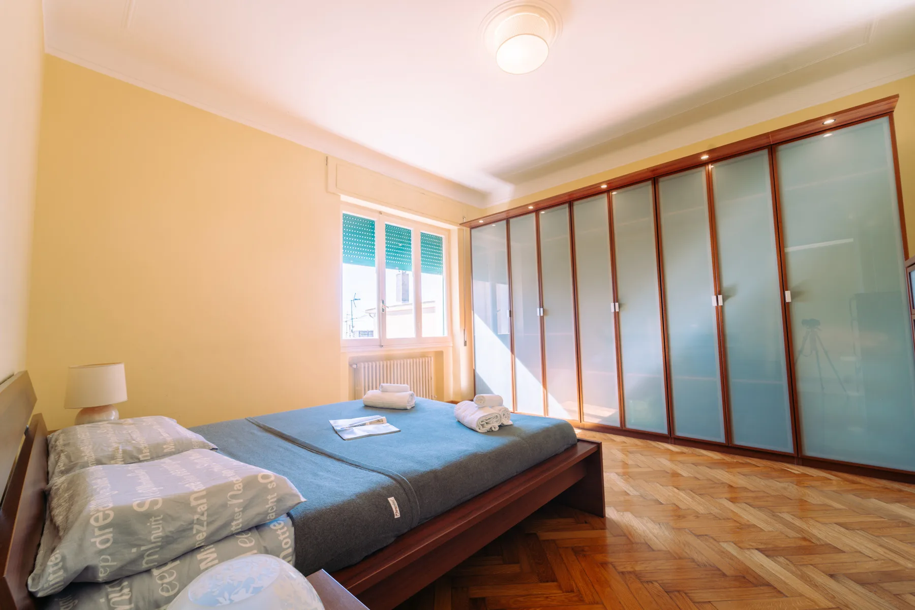 A bedroom with beds beside a large wardrobe and a window.