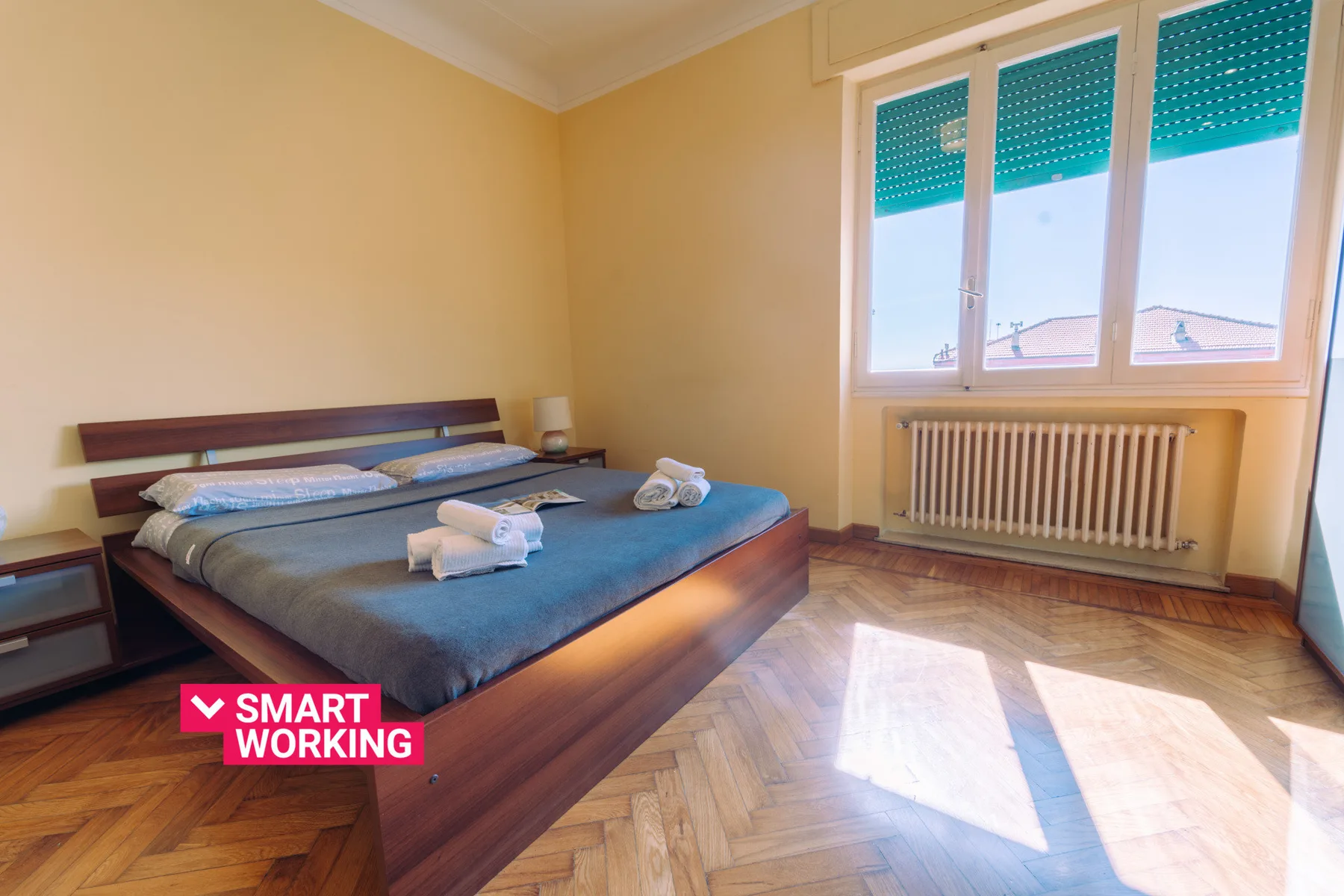 A bedroom with a bed beside a large window and radiator.