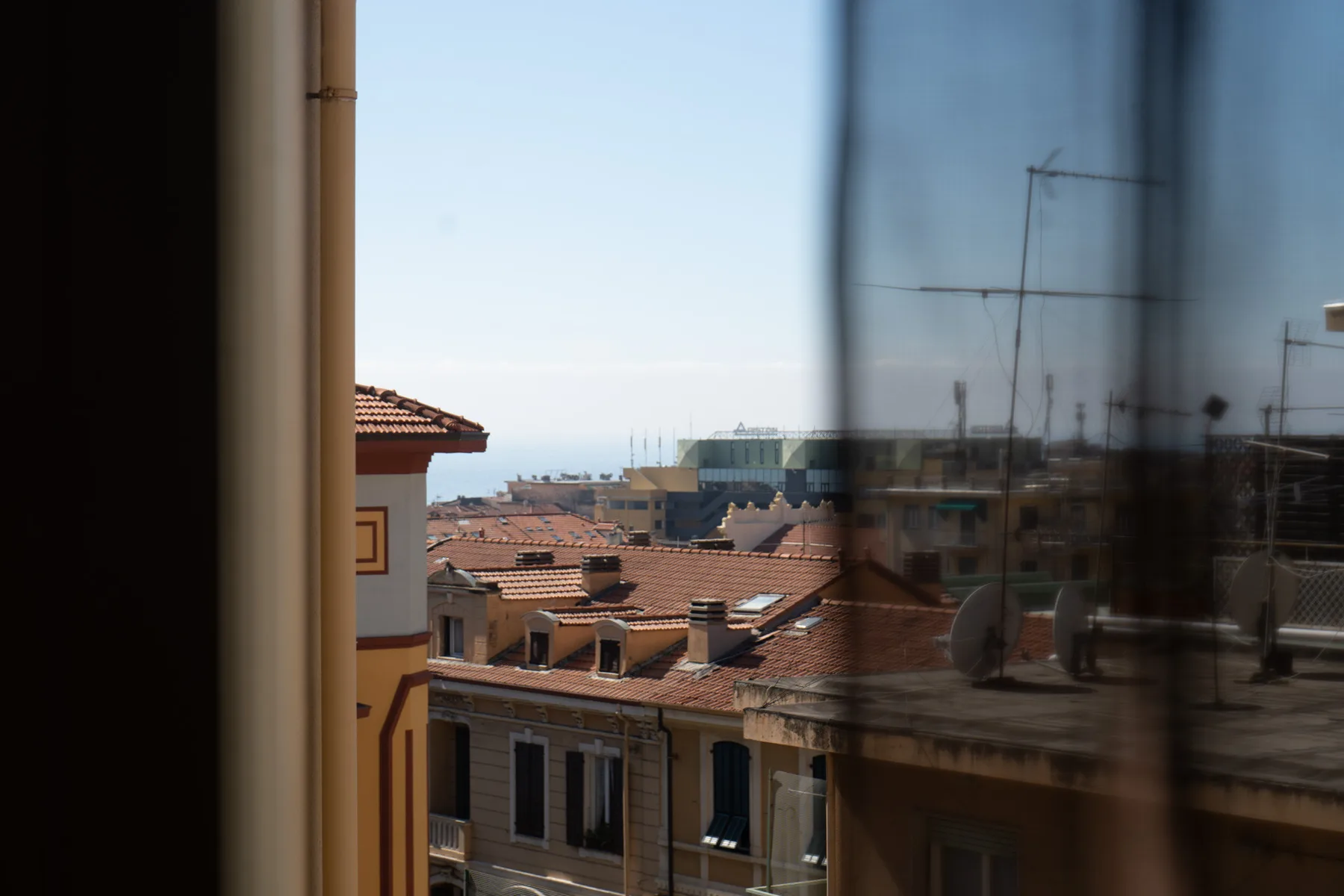 A city view through a window, with terracotta rooftops and distant buildings.