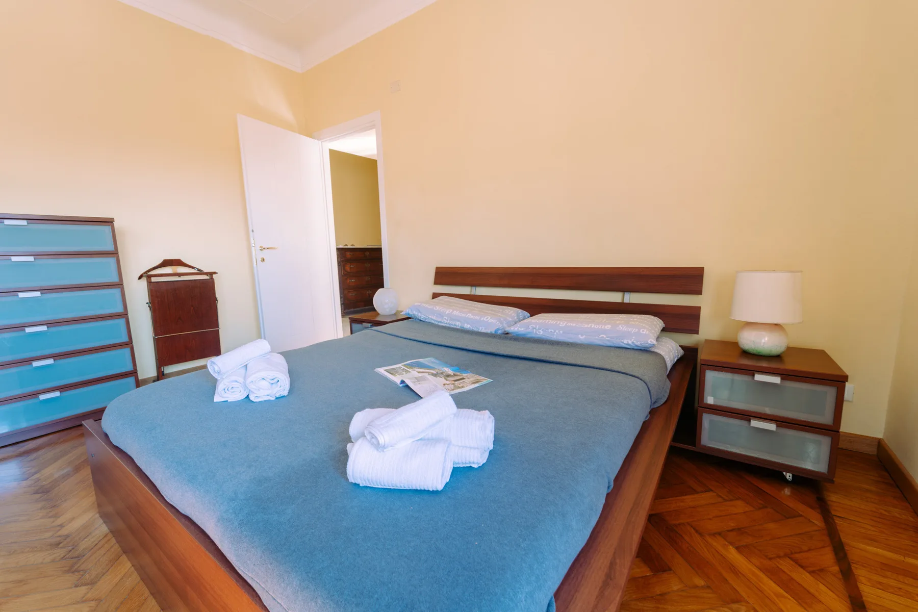 A bedroom with a large bed, blue bedding, and a bedside lamp.