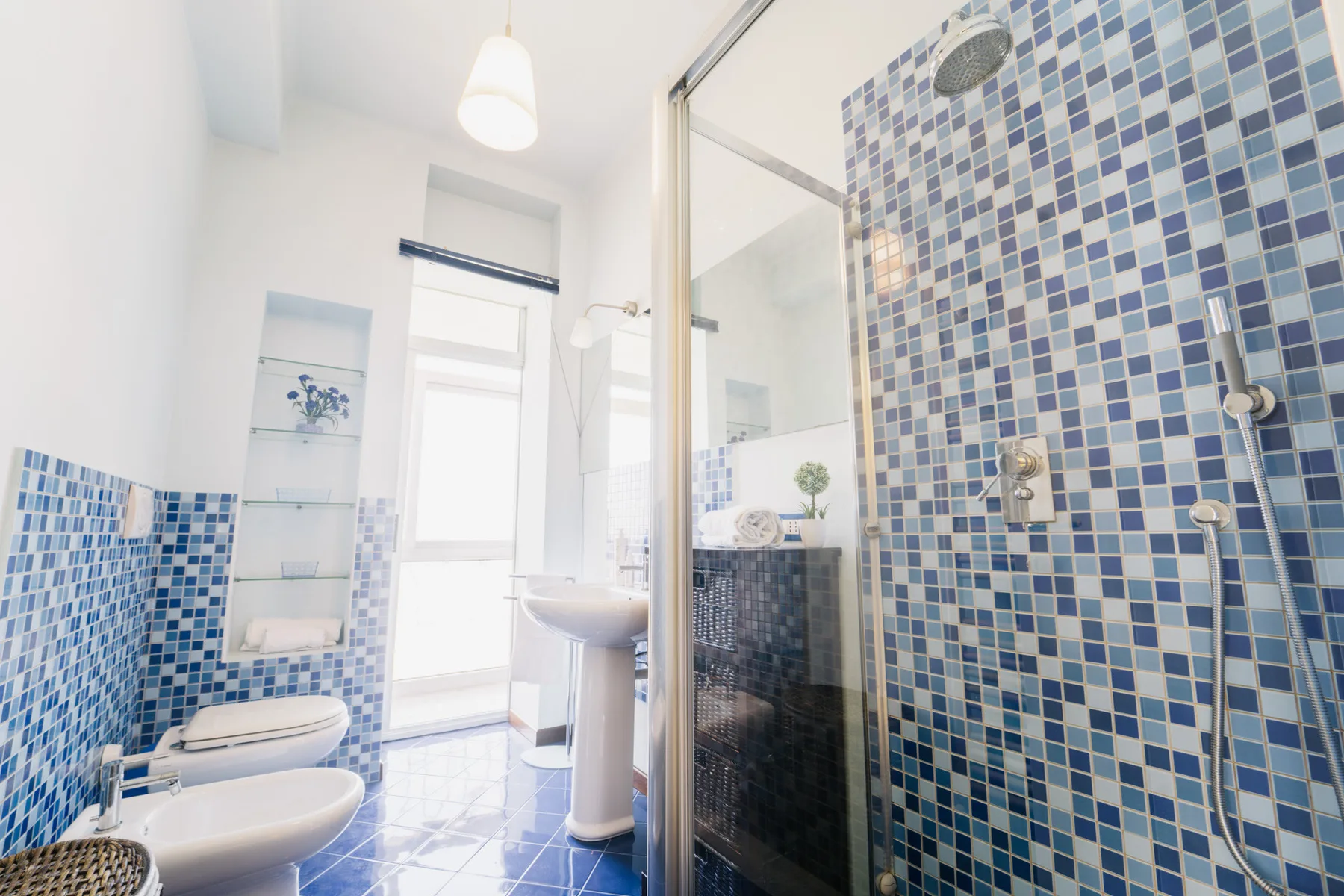 A bright tiled bathroom with a glass shower and white bathroom fixtures.