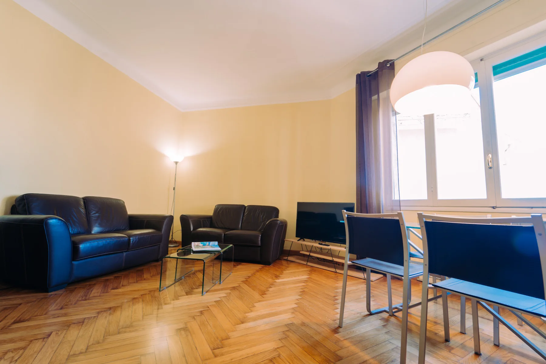 Una sala de estar con asientos oscuros, una mesa de centro y un comedor junto a las ventanas.