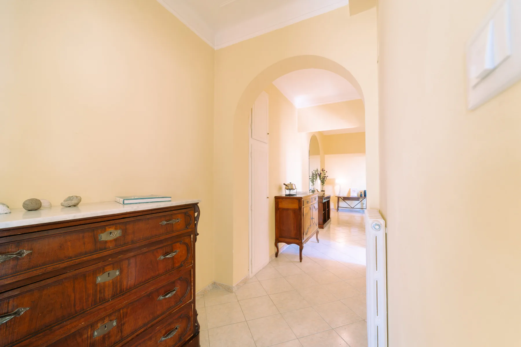 A warm-toned interior hallway opens through an archway into a furnished room.