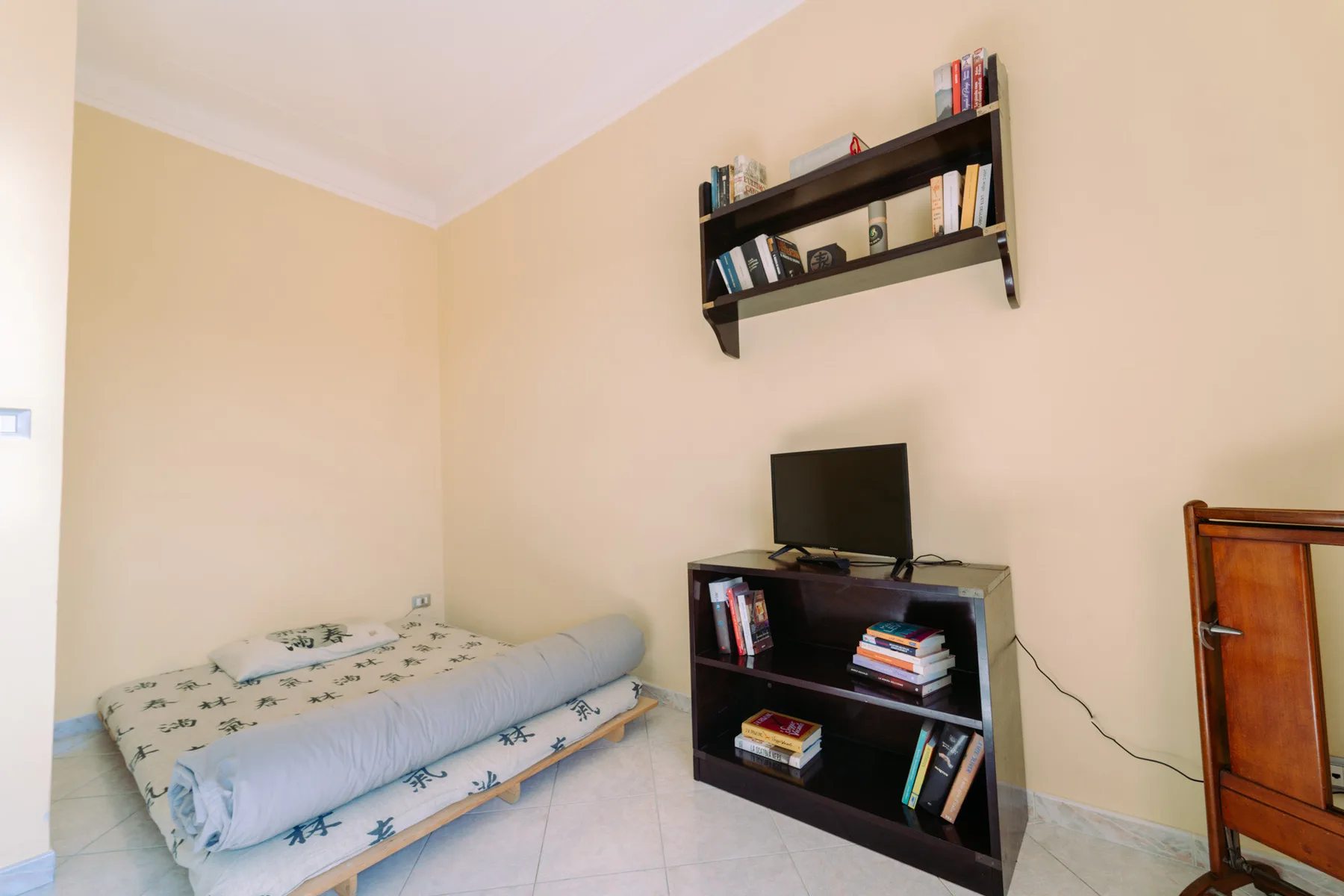 Un dormitorio con una cama baja, un televisor y estantes en la pared.