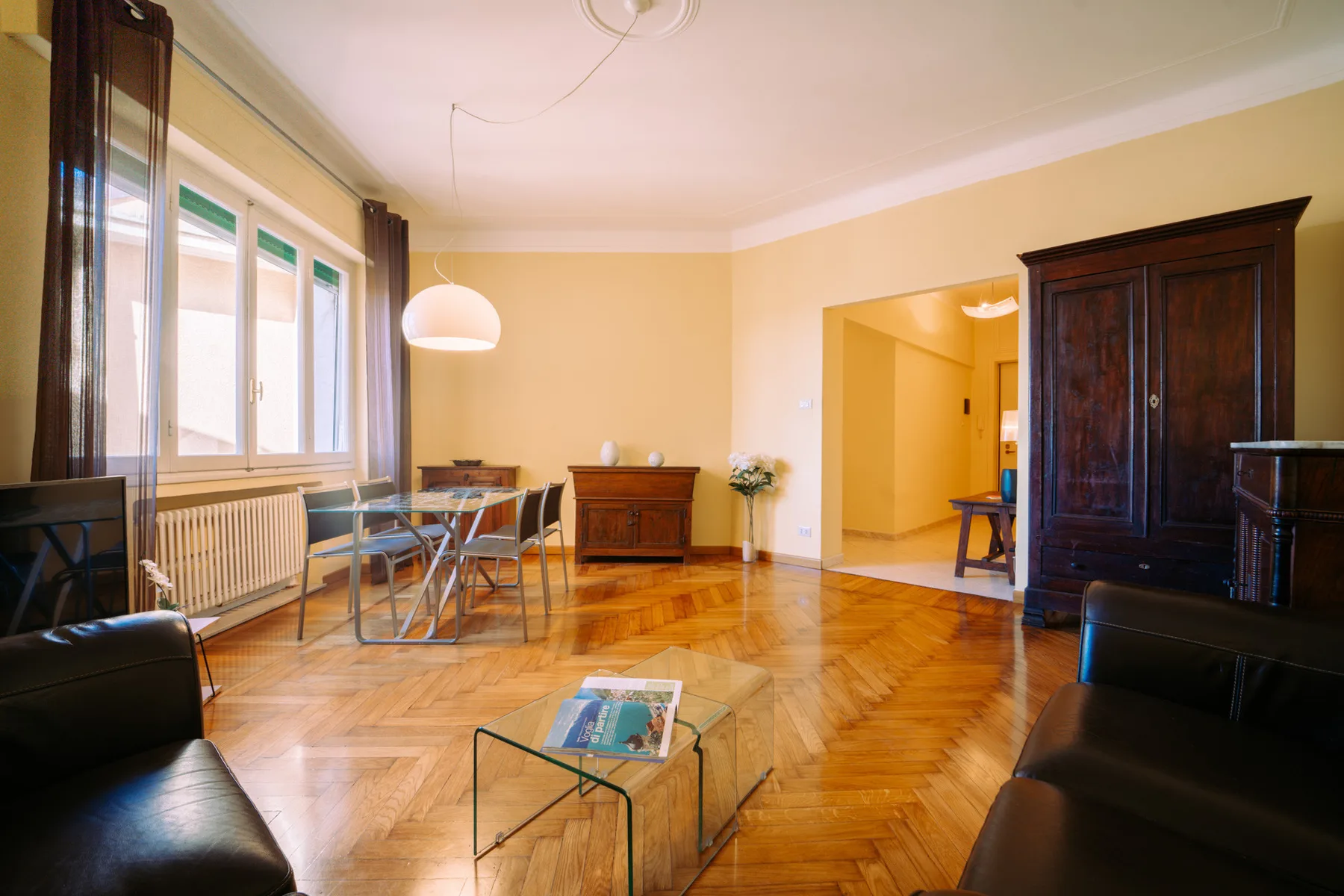 Una sala de estar con asientos, una mesa de centro de vidrio y ventanas altas.