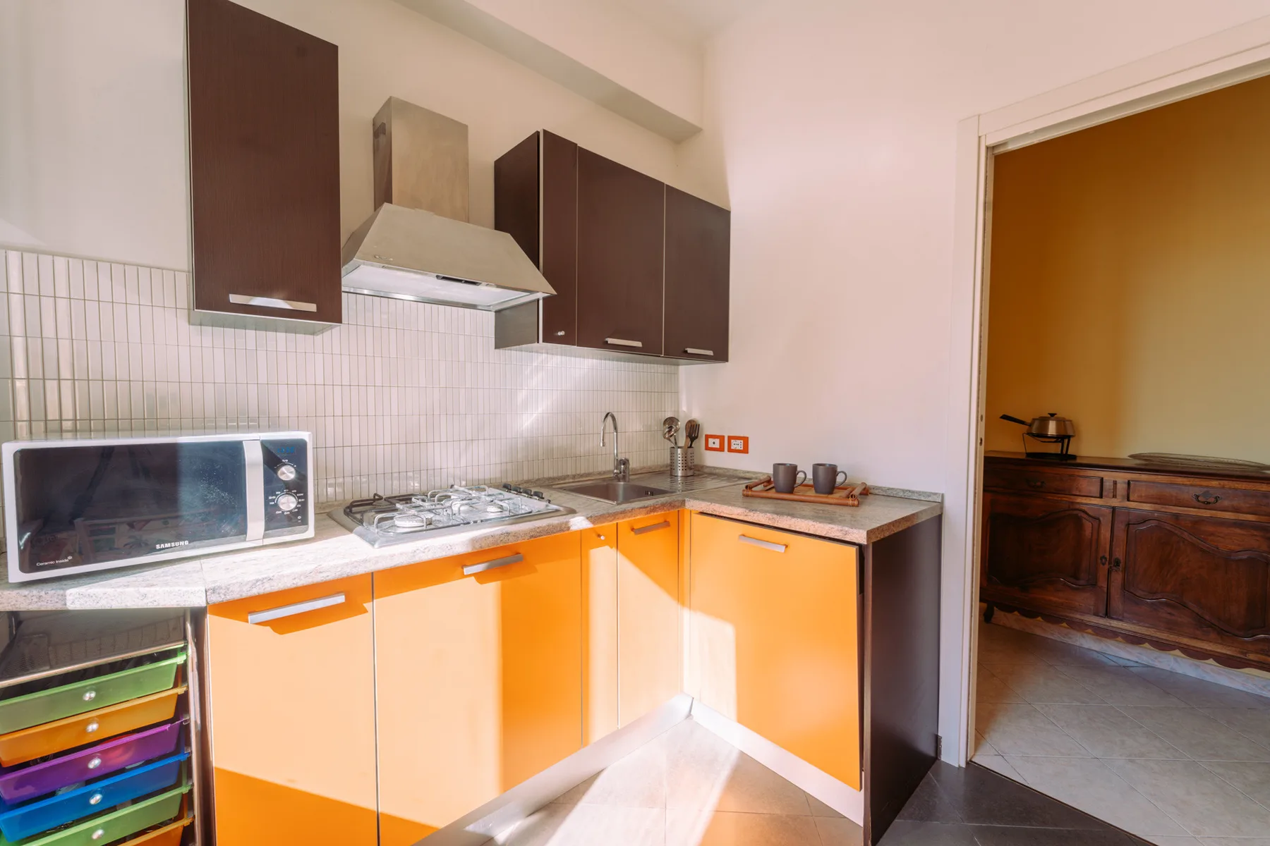 A compact kitchen with orange lower cabinets, a cooktop, and a microwave.