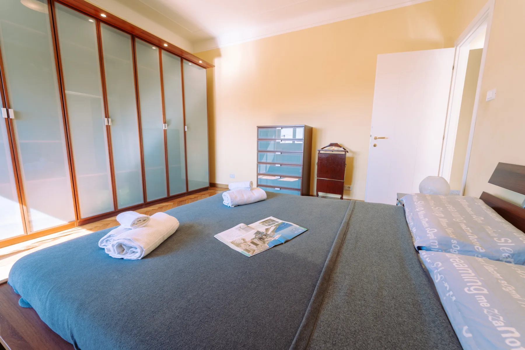 A bedroom with a large bed, wardrobe, and small storage cabinets.