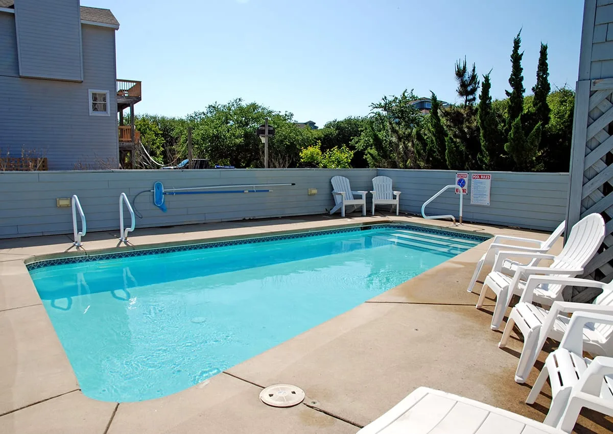 Una piscina al aire libre está rodeada por una terraza pavimentada y asientos.