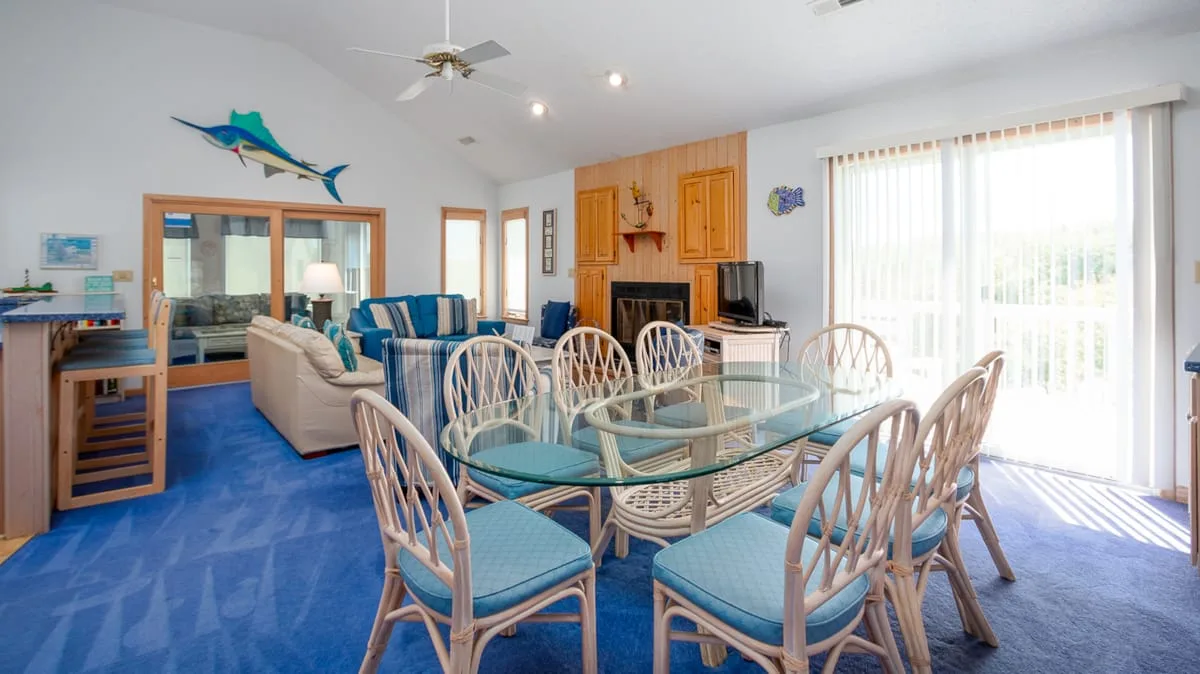 Una luminosa sala de estar y comedor con una mesa de vidrio y alfombra azul.