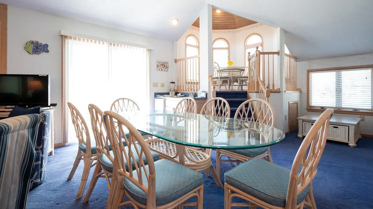 A dining area with a glass table and seating beside a raised sitting space.