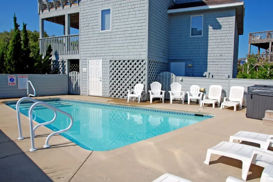 Una piscina exterior junto a una casa, con tumbonas a lo largo de la terraza.