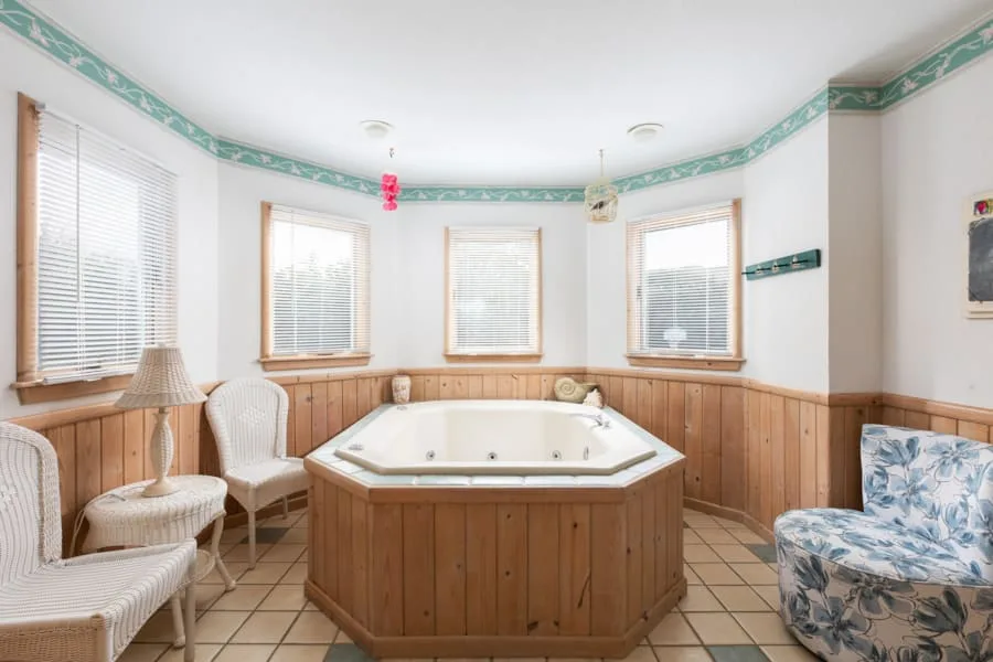 Una habitación luminosa cuenta con una bañera esquinera grande, ventanas y asientos.