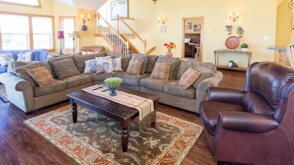 A spacious living room features sectional seating, a coffee table, and a staircase.