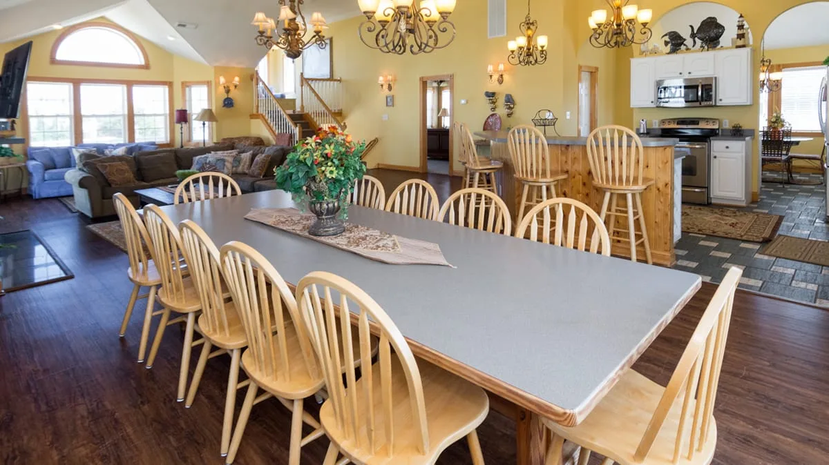 An open dining and kitchen area features a long table and wooden seating.