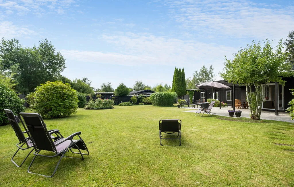 A grassy garden with outdoor seating and a low building beneath a partly cloudy sky.