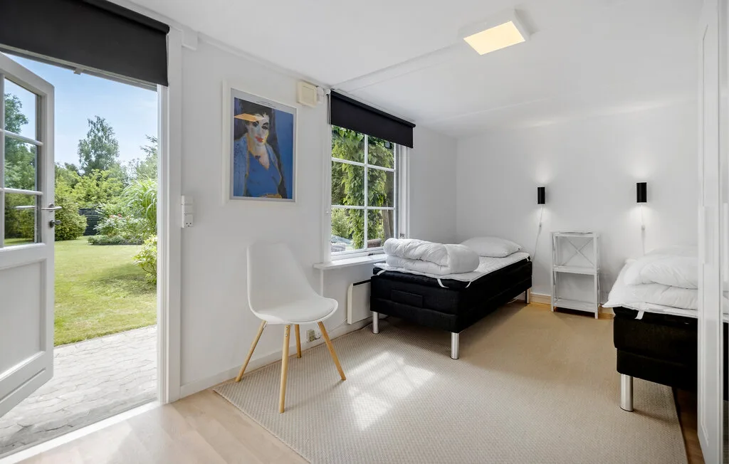 A bright bedroom with two beds, a desk, and a garden view through open doors.