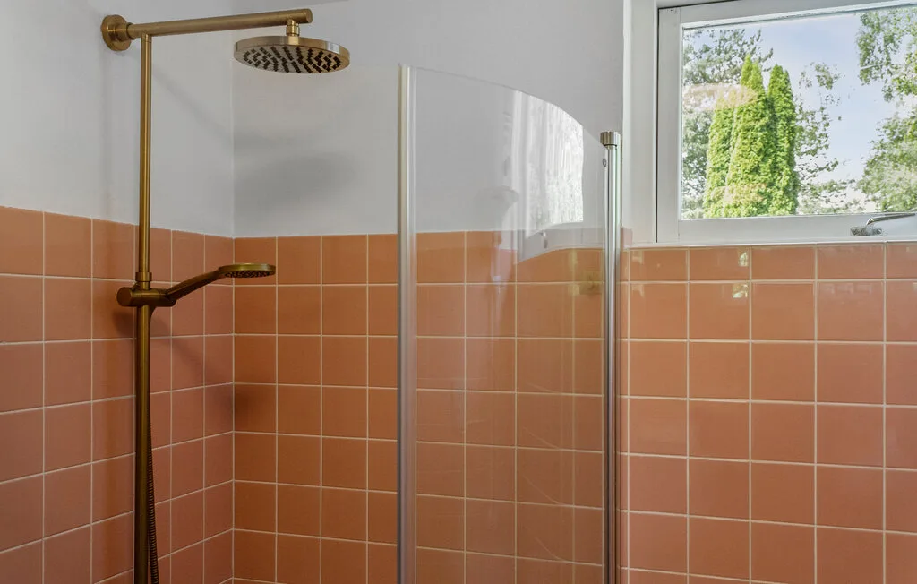 A tiled shower area with brass fixtures and a window above the wall.