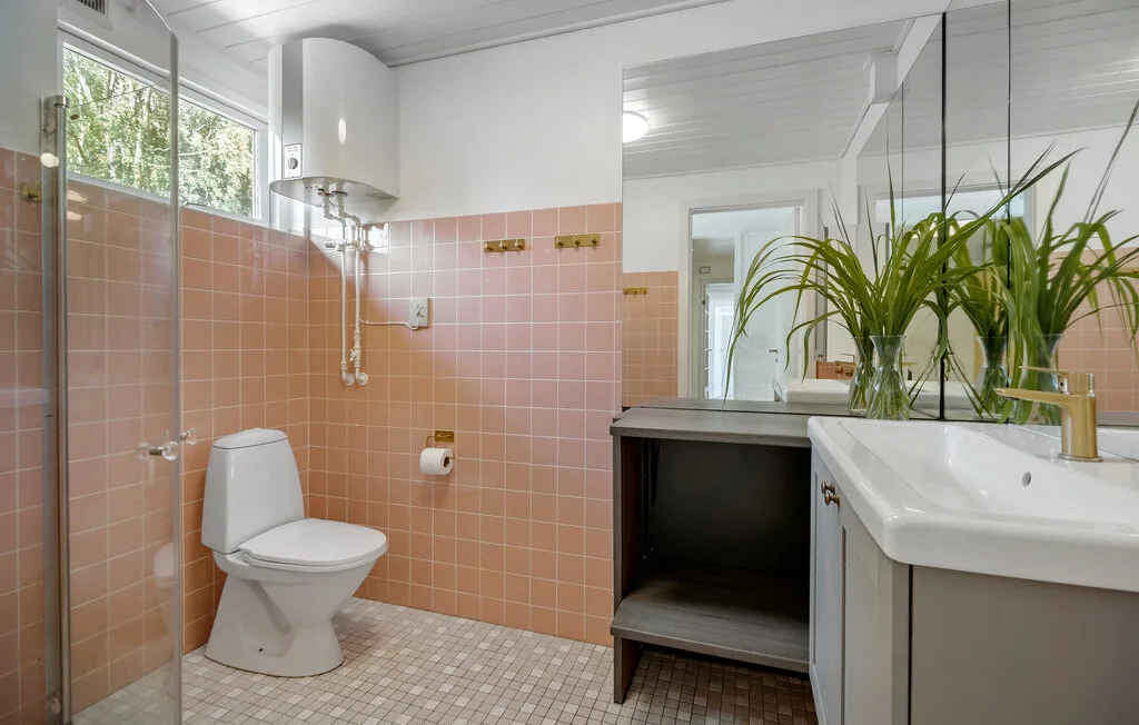 A tiled bathroom with a toilet, vanity, and leafy plants.