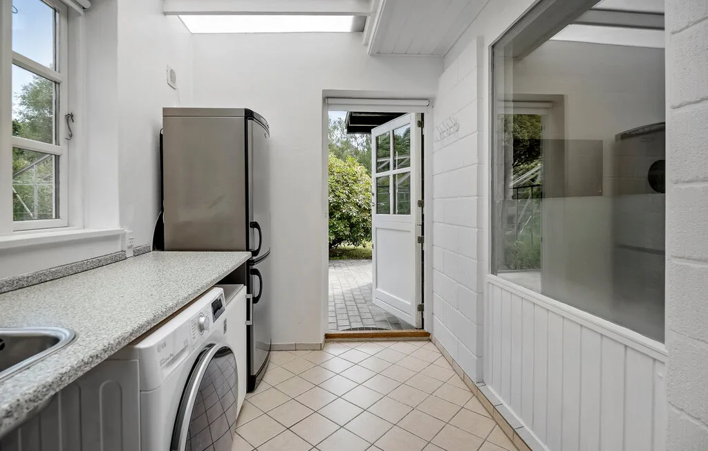 A bright utility room with laundry appliances and a counter beside an open garden door.