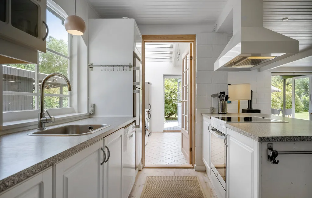 A bright kitchen with white cabinetry, a sink, and a central doorway.