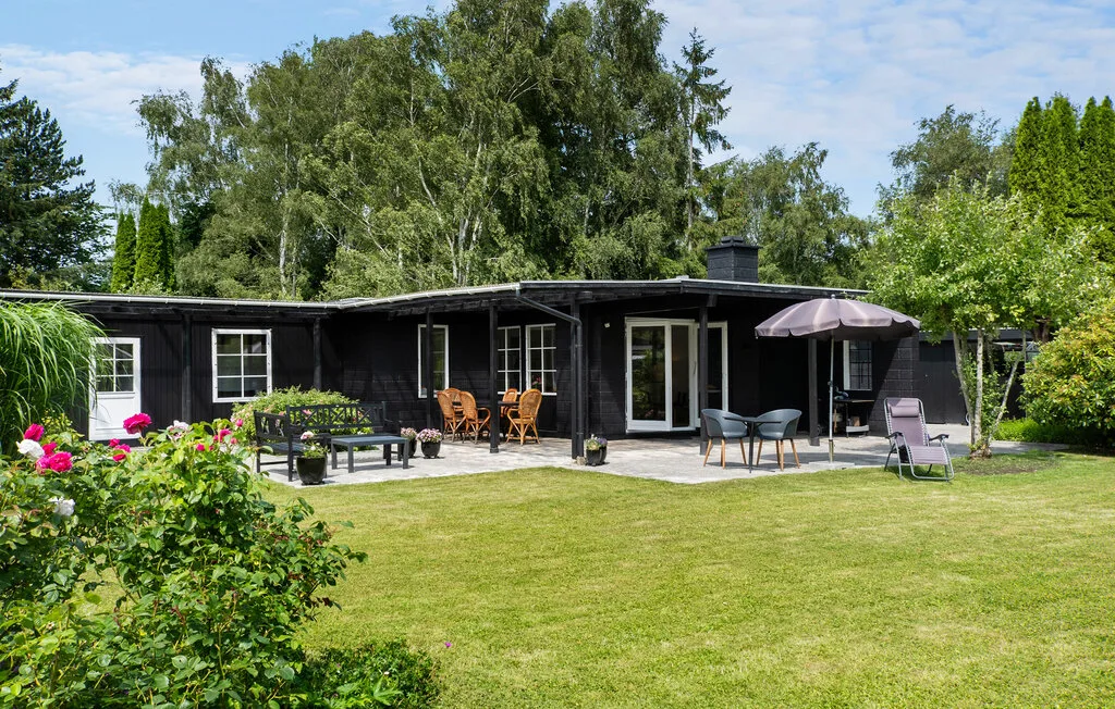A low house opens onto a patio with outdoor seating and a garden lawn.