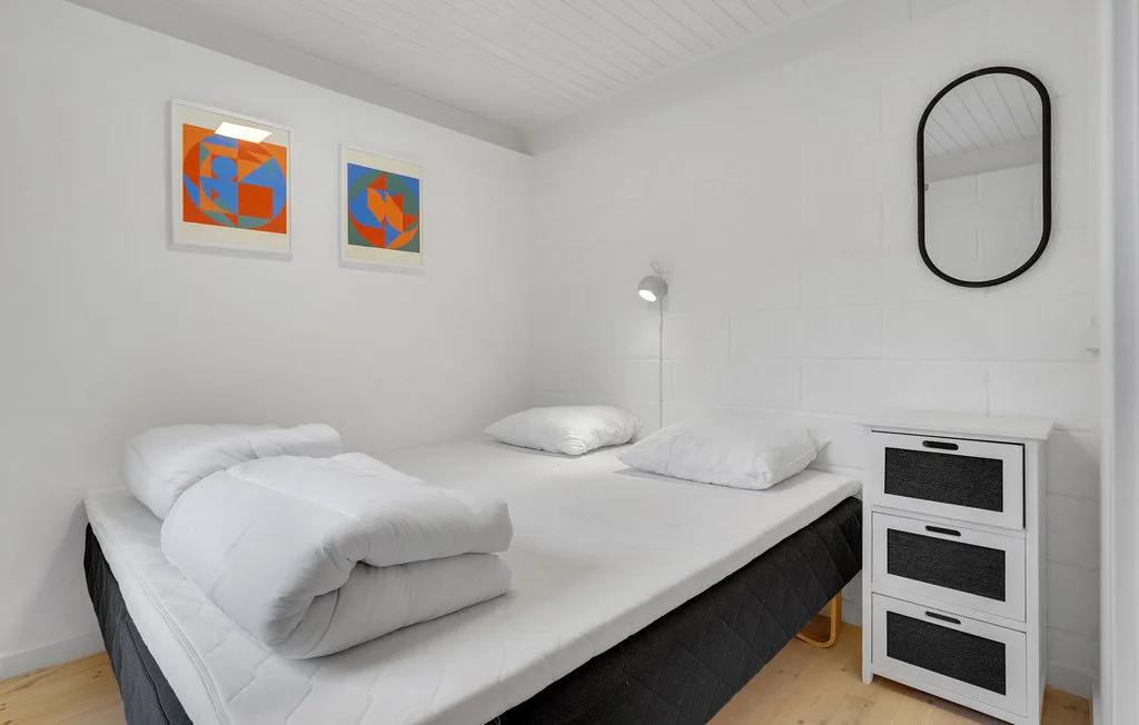 A bright bedroom with white bedding, colorful wall art, and a chest of drawers.