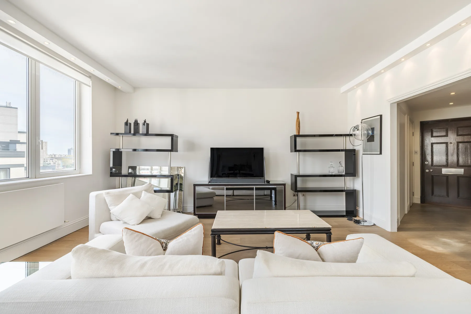 A bright living room with white seating, a coffee table, and a television.