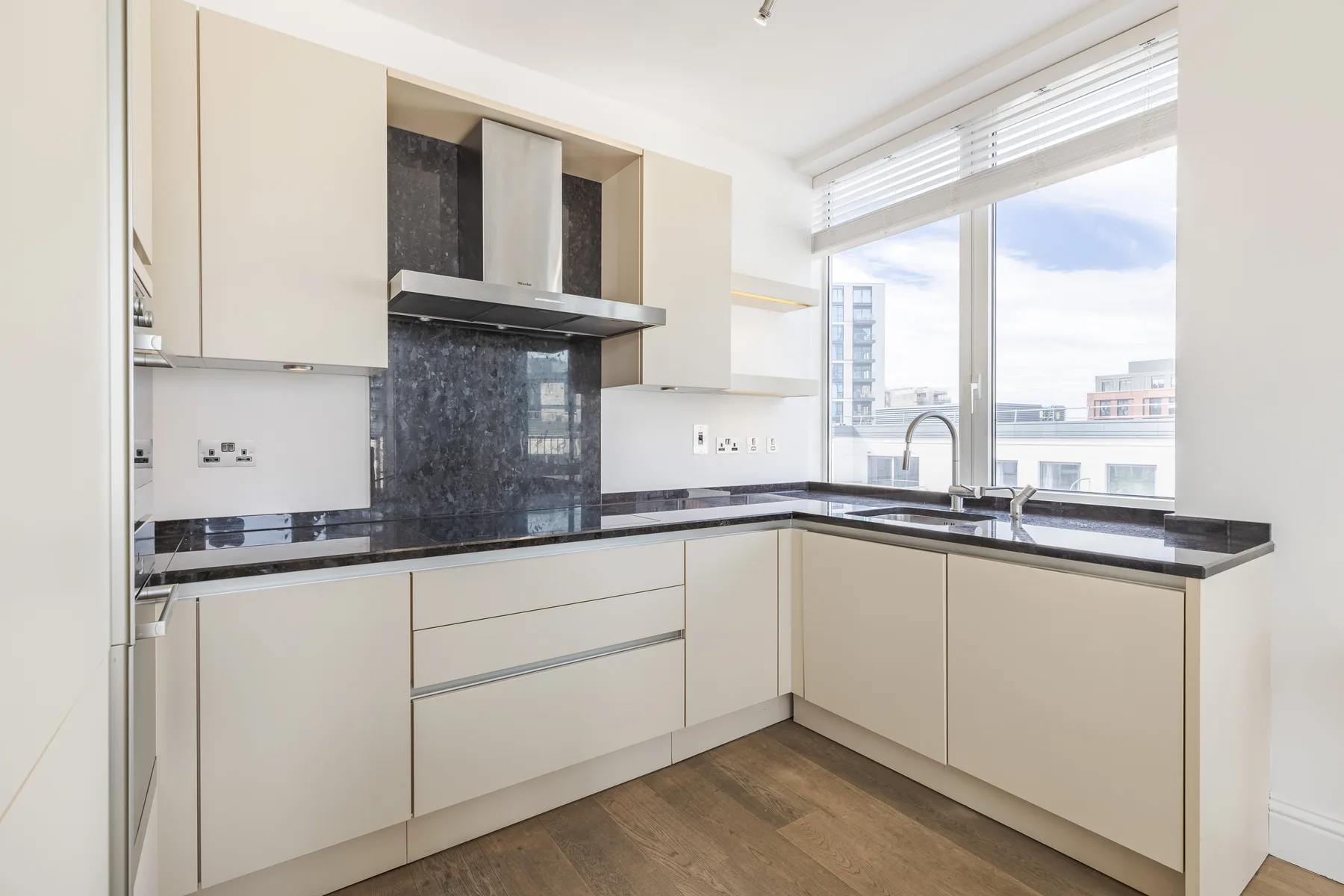 A bright kitchen with pale cabinets, dark countertops, and a large window.