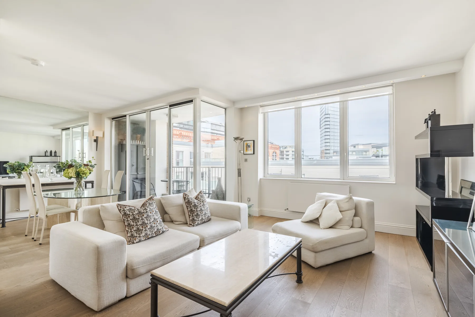 A bright living room with seating beside large windows and an open dining area.