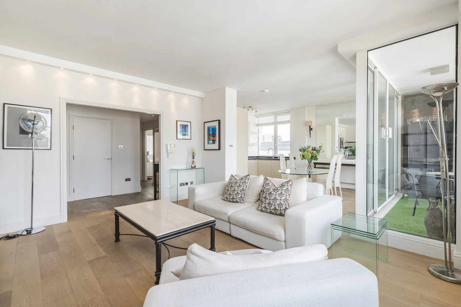A bright living room with white seating and a glass coffee table.