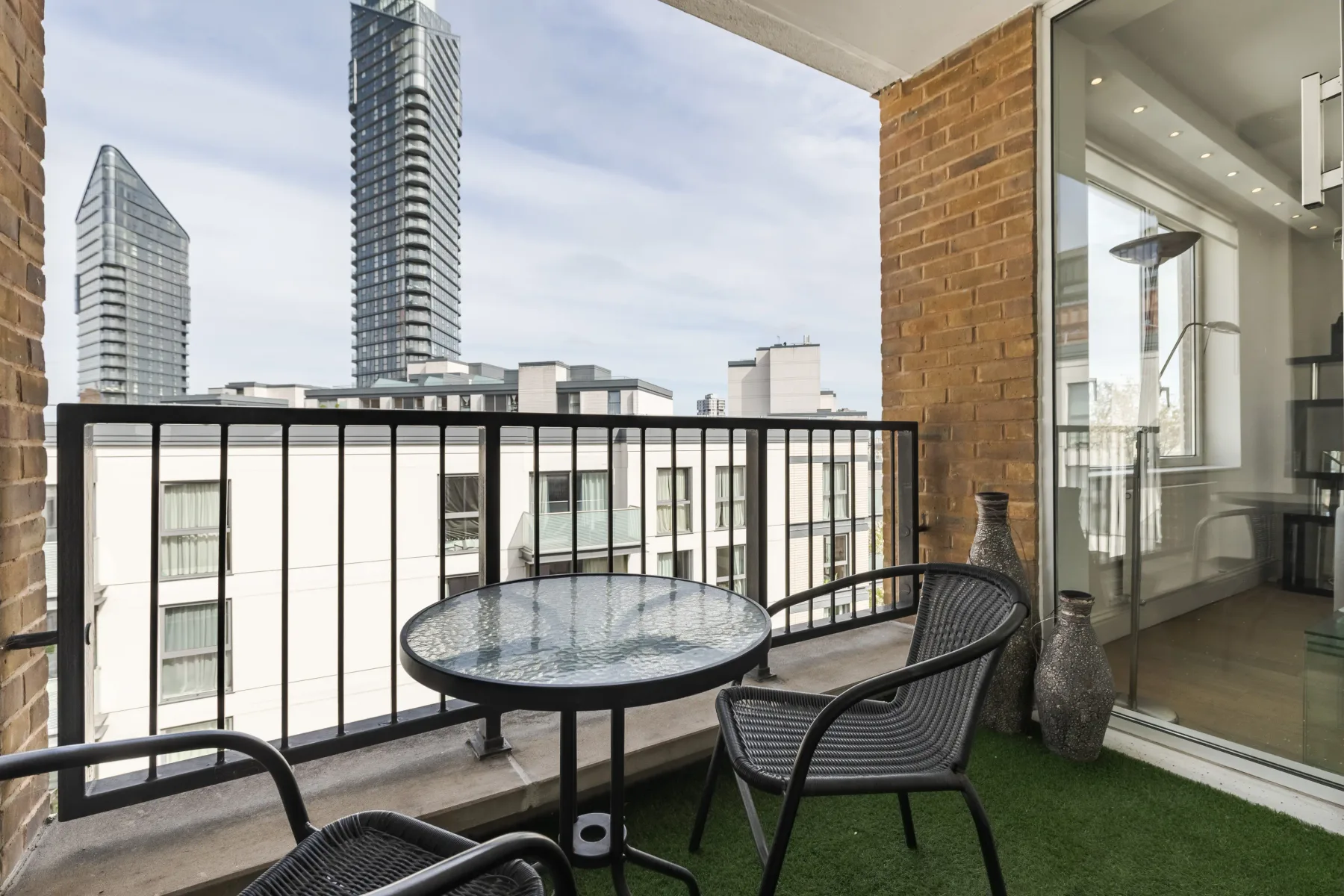 A balcony seating area overlooks nearby buildings through a black railing.