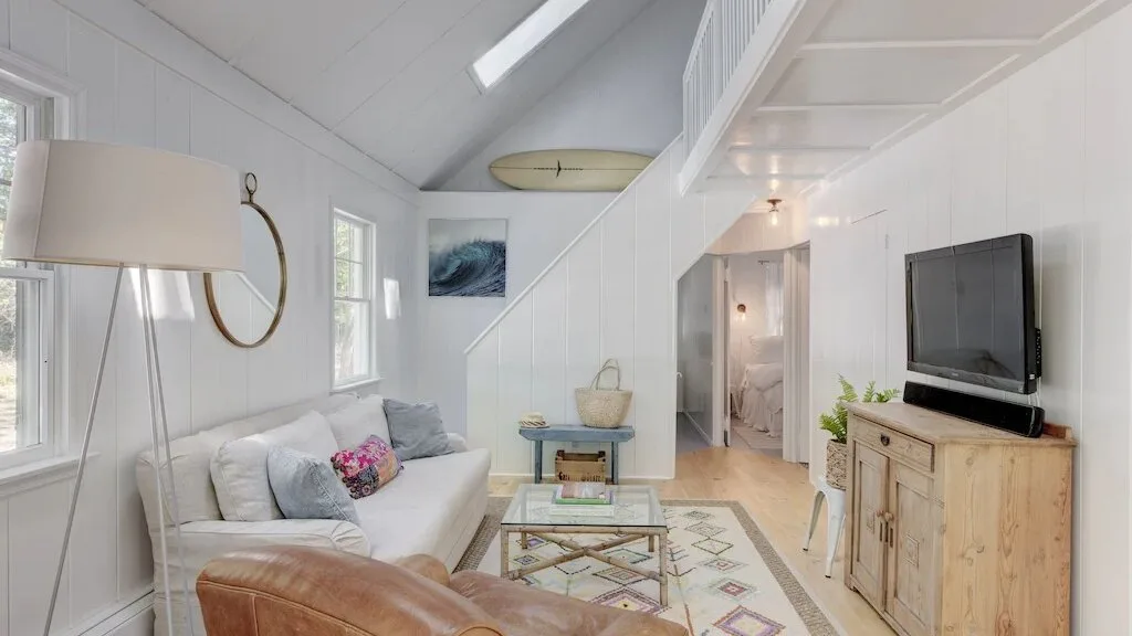 A bright living area with seating, a television, and a glass coffee table.