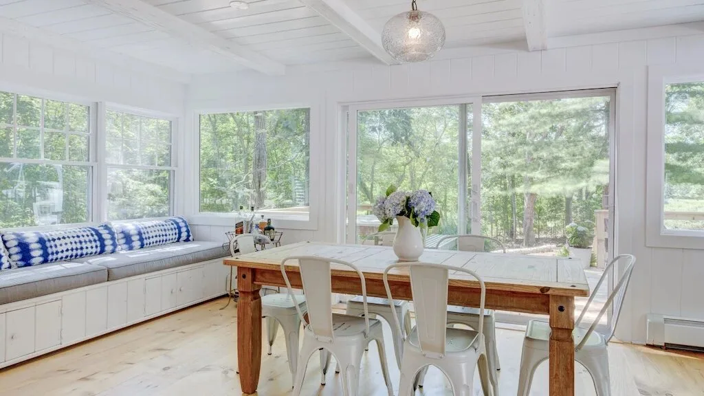 Un comedor luminoso con una mesa larga y ventanas con vistas a la vegetación.