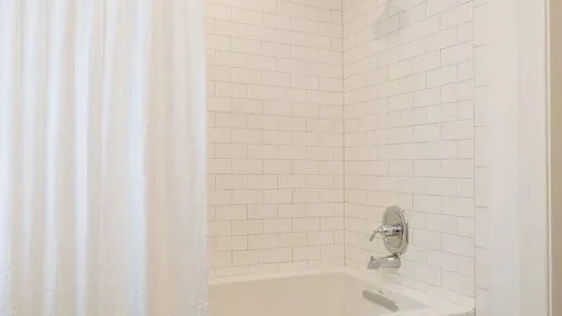 Una zona de ducha con azulejos, cortina blanca y accesorios en la pared.