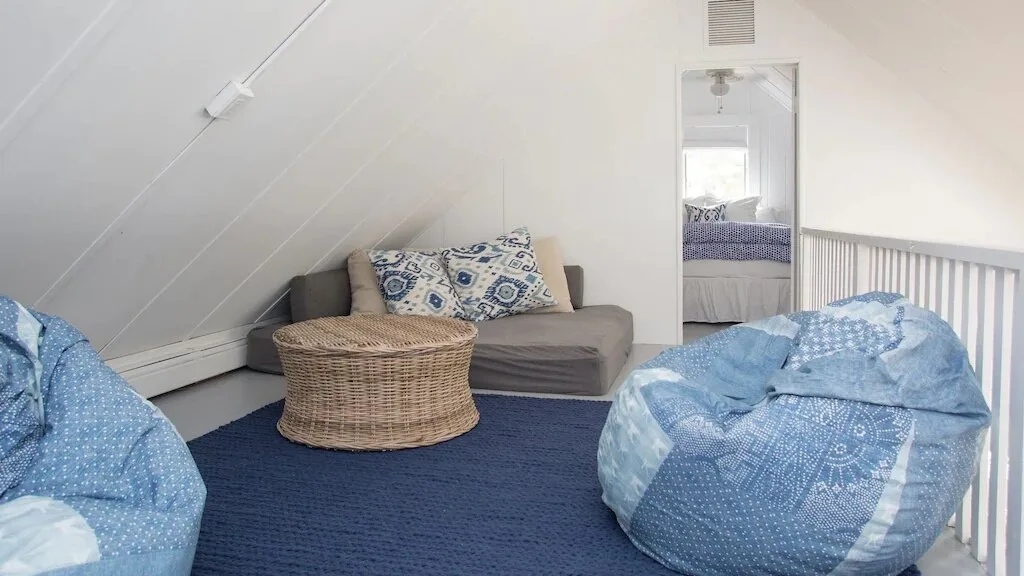 Un dormitorio abuhardillado luminoso con ropa de cama azul y una pequeña zona de descanso.