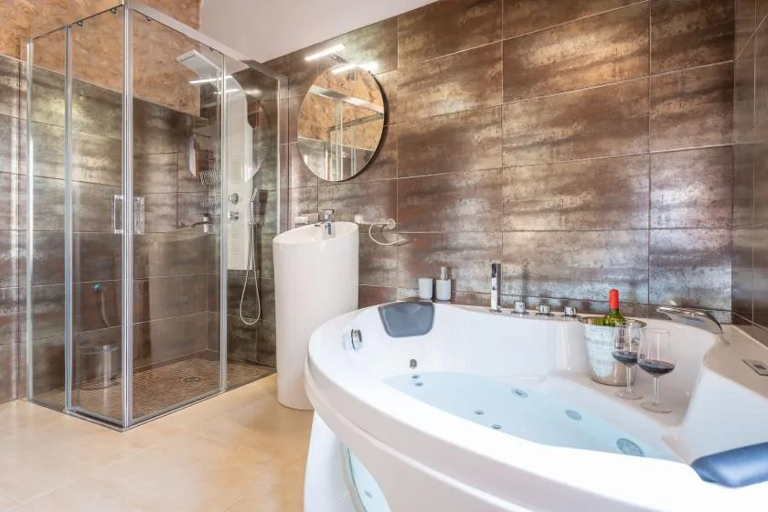 A bathroom with a glass shower, round mirror, and large soaking tub.