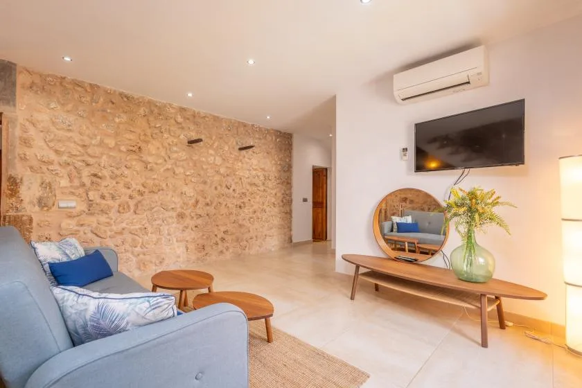 A bright living room has a stone wall, seating, and a wall-mounted television.